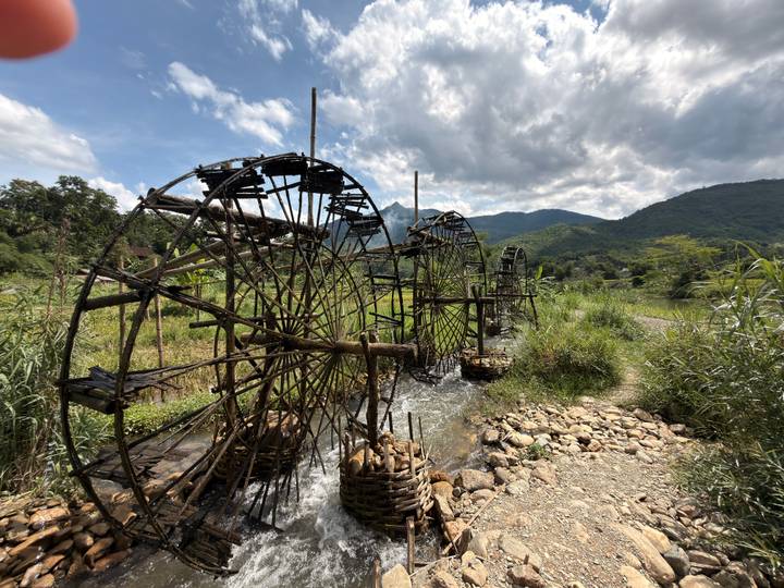 Series of rustic bamboo water wheels channel mountain stream water beside lush green valley.