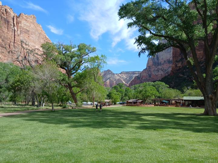 Green meadow surrounded by towering sandstone cliffs and cottonwood trees in bright spring weather.