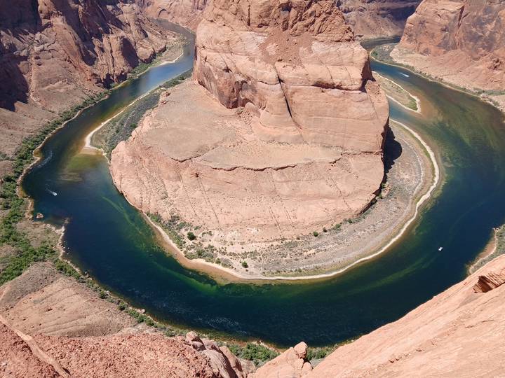 Overhead view of the dramatic horseshoe bend of a deep blue river curving around a sandstone mesa.