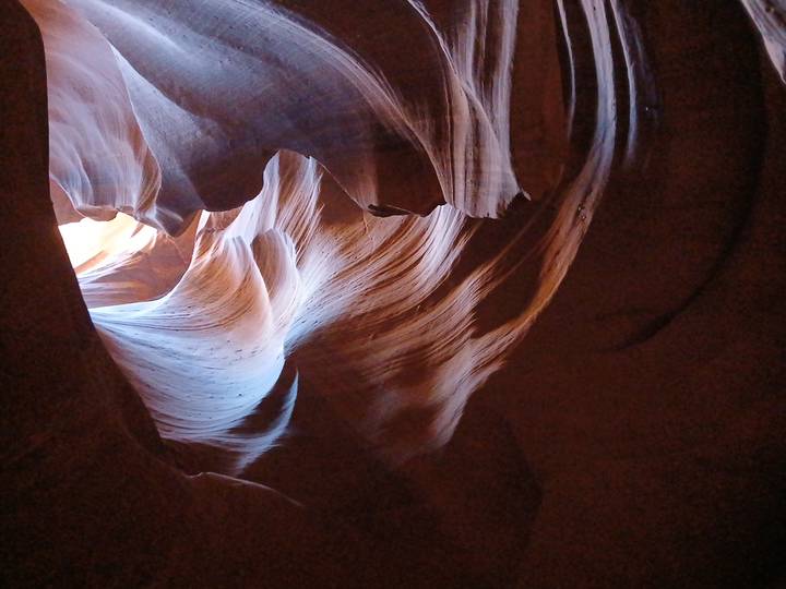 Sunlight streams through swirling, wave-like walls inside a narrow sandstone slot canyon.