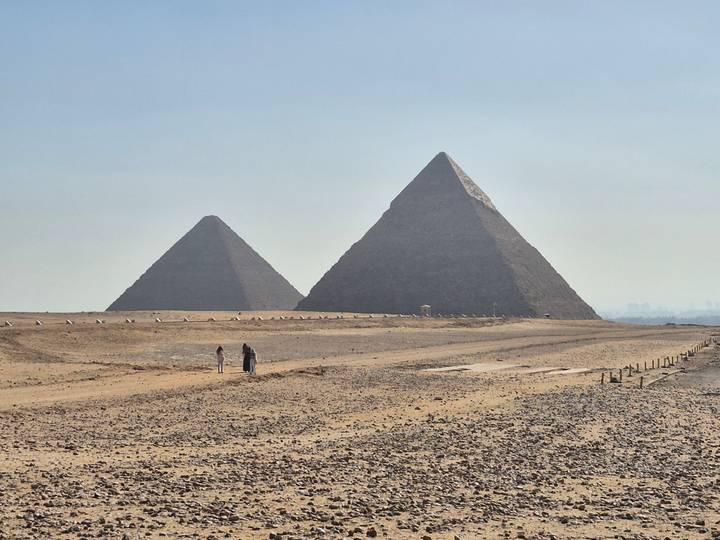 Two prominent pyramids rising above the desert sands under a hazy blue sky.
