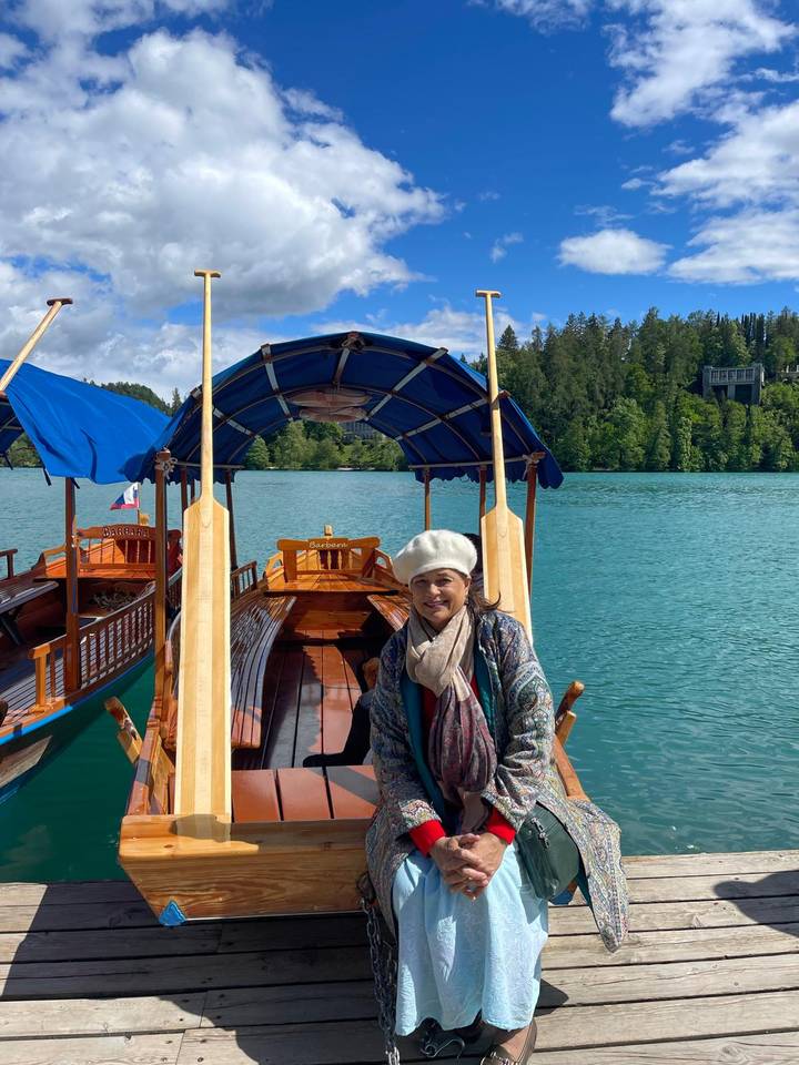 Smiling traveller stands beside a traditional wooden pletna boat on turquoise Lake Bled