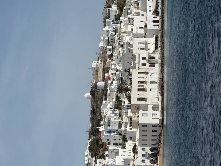 Seaside view of whitewashed Cycladic buildings and a classic windmill overlooking the Aegean in Mykonos.