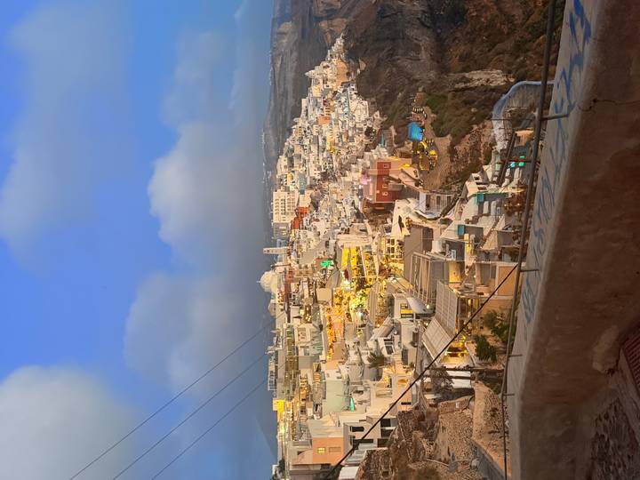 Elevated evening view of colorful cliff-side houses and caldera in Santorini under a blue twilight sky.