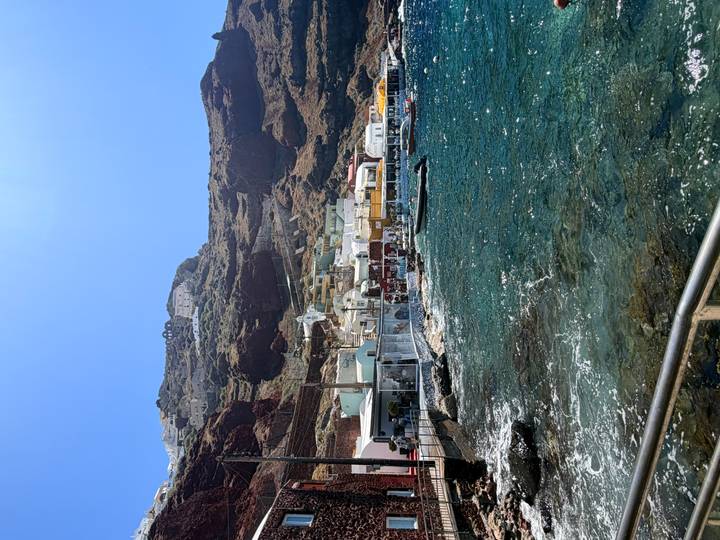 Seaside village with colorful houses built into steep volcanic cliffs beside sparkling blue water.