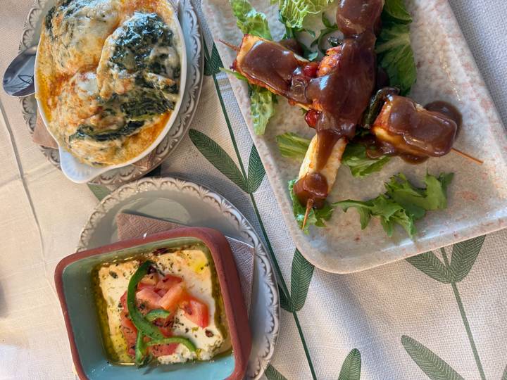 Close-up of traditional Greek dishes including baked feta, spinach gratin and meat in sauce on a rustic table.