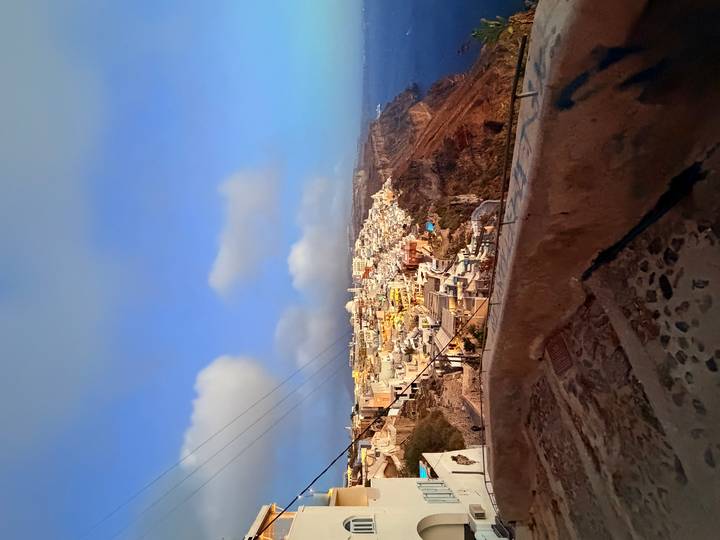 Wide view of Santorini’s cliff-side town glowing with early morning light above the Aegean Sea.