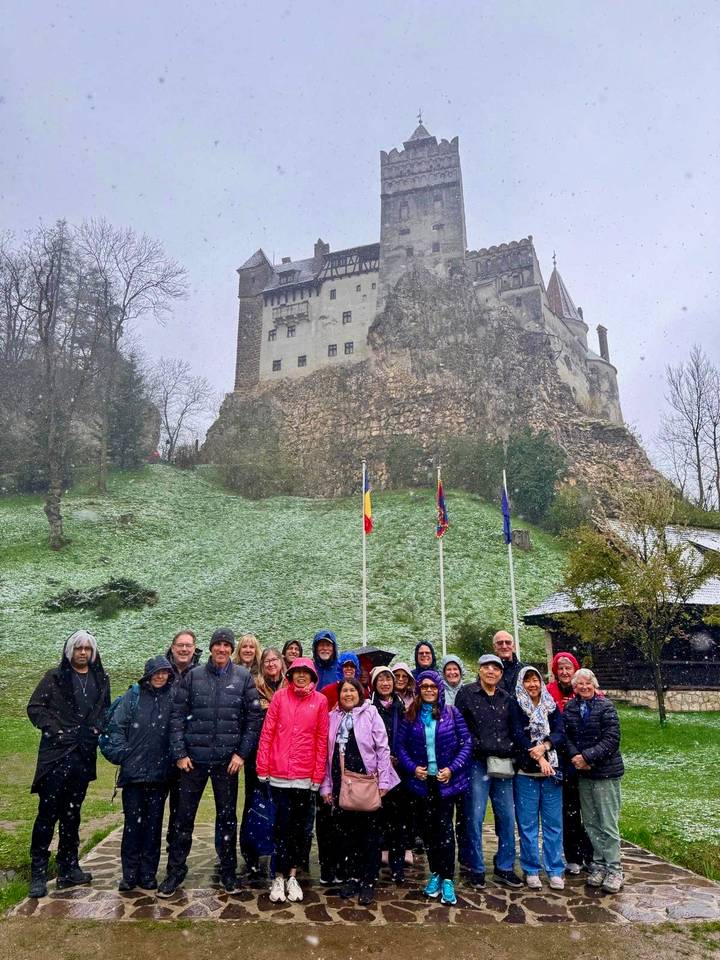 A tour group poses in falling snow below the dramatic walls and towers of Bran Castle.