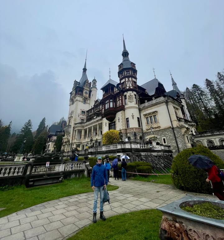 Grand Neo-Renaissance Peles Castle stands amid misty forested hills while visitors explore the grounds.