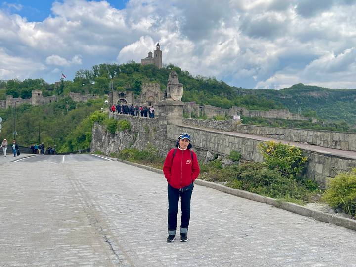 A traveller smiles on a cobbled road leading to the hilltop Tsarevets Fortress dotted with visitors.