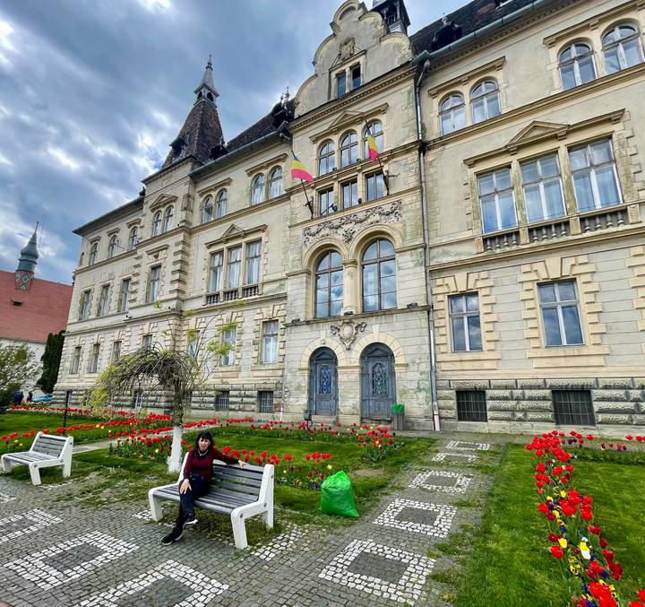 An ornate historic building fronted by red tulip beds is enjoyed by a seated visitor.