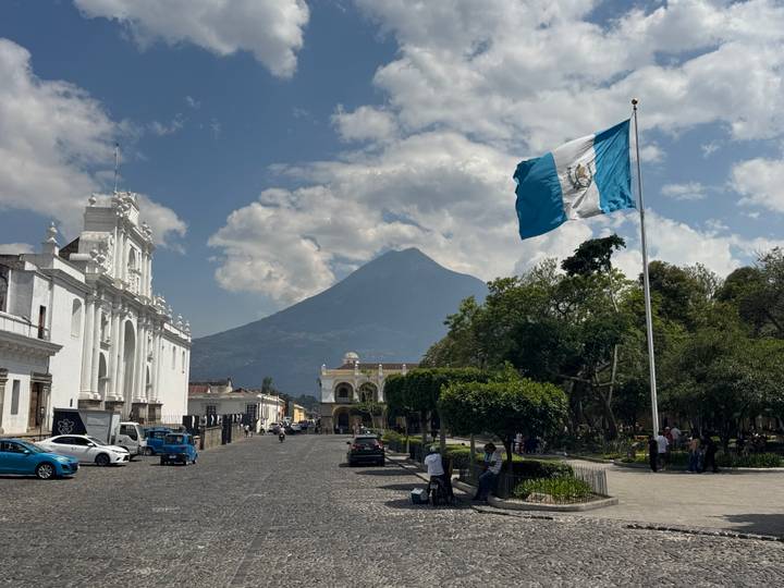 Guatemala’s blue-white flag waves over Antigua’s plaza with Volcán de Agua rising in the background.