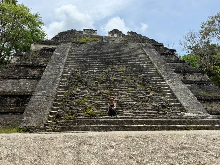 A lone visitor sits on the massive stone staircase of an ancient Maya pyramid in Tikal.