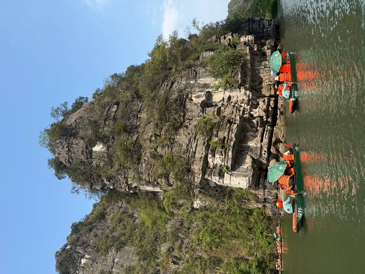 Limestone karst cliffs rising above green water with small tour boats below.