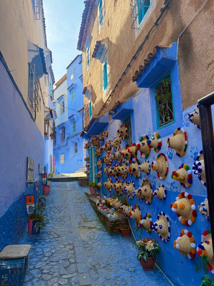 Narrow alley of bright blue buildings in Chefchaouen with colorful woven hats decorating the walls