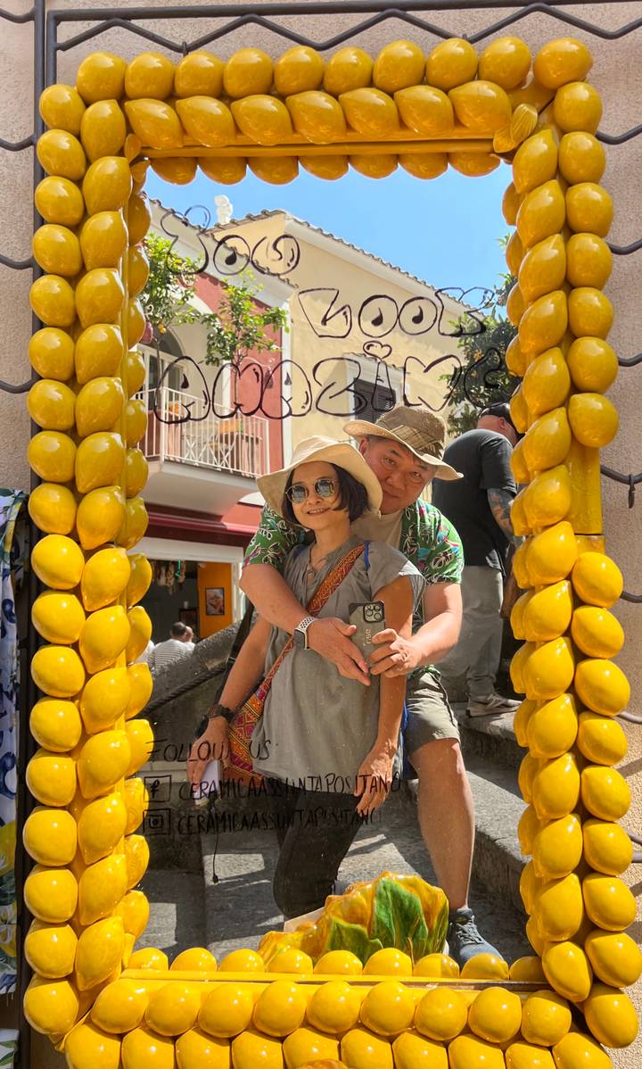 Couple posing inside decorative lemon-themed frame in sunny Italian street.
