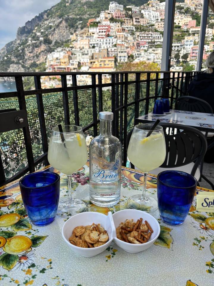 Two lemon spritz cocktails and a bottle of sparkling water on ceramic-tiled café table.