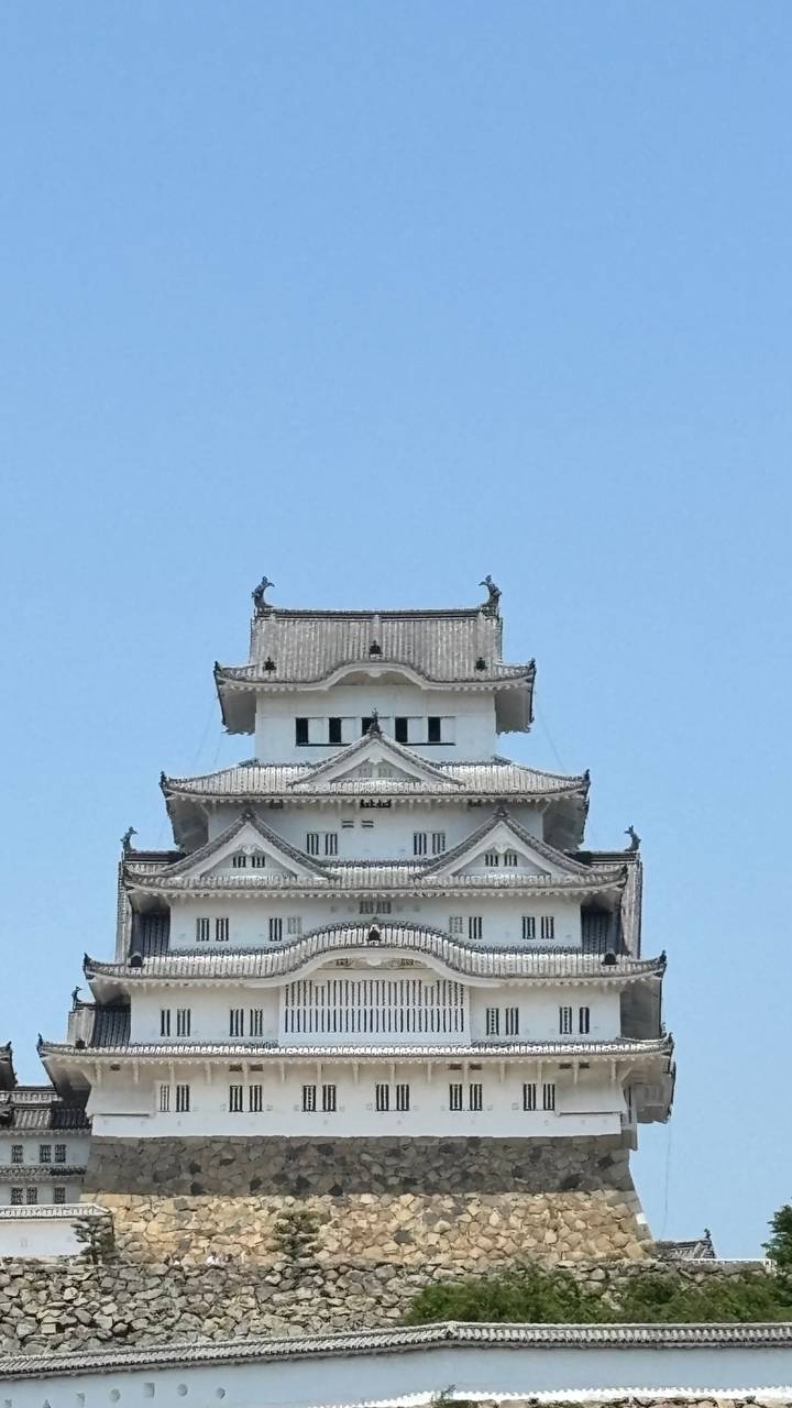 Close-up of white timber roof tiers of Himeji Castle against clear blue sky.
