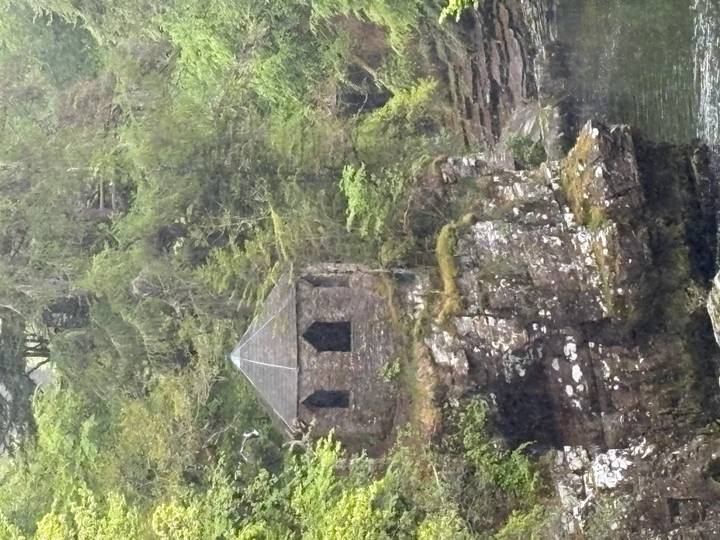 Small stone gazebo nestled on a mossy cliff in a lush Scottish forest.