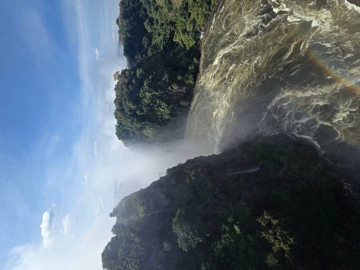 Powerful Victoria Falls with mist rising between lush cliffs and a faint rainbow below.