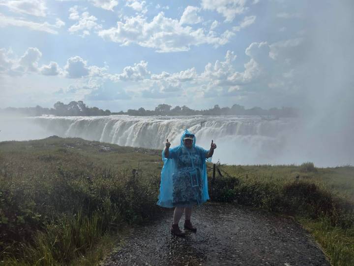 Traveller in blue rain poncho posing in front of mist-shrouded Victoria Falls.