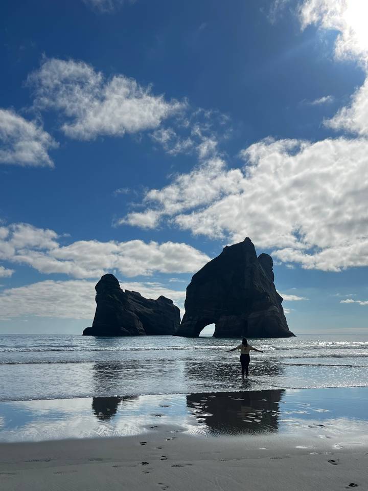 Dramatic twin sea stacks rising from calm ocean under bright blue sky with scattered clouds