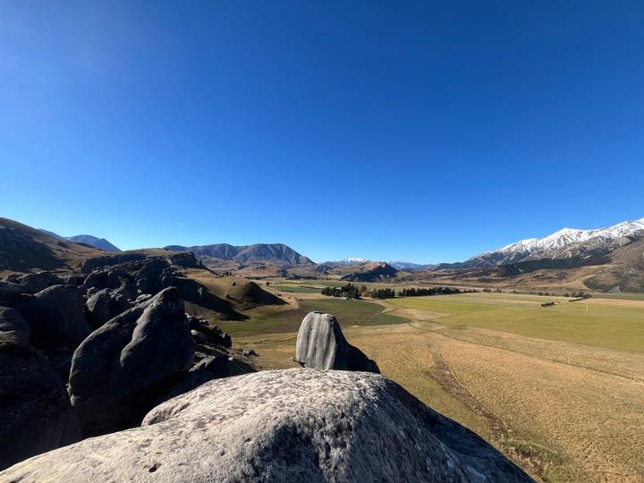 Panoramic view of New Zealand high country valleys framed by large grey boulders in foreground