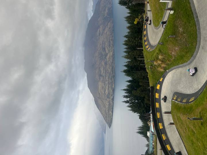 Winding luge track descending green hillside overlooking lake and forest in Queenstown