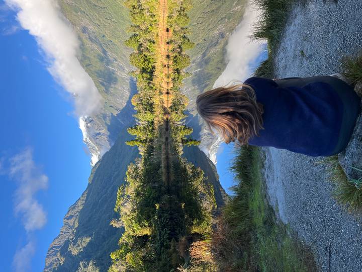 Traveller sitting by mirror-like lake reflecting snowy peak near Franz Josef Glacier