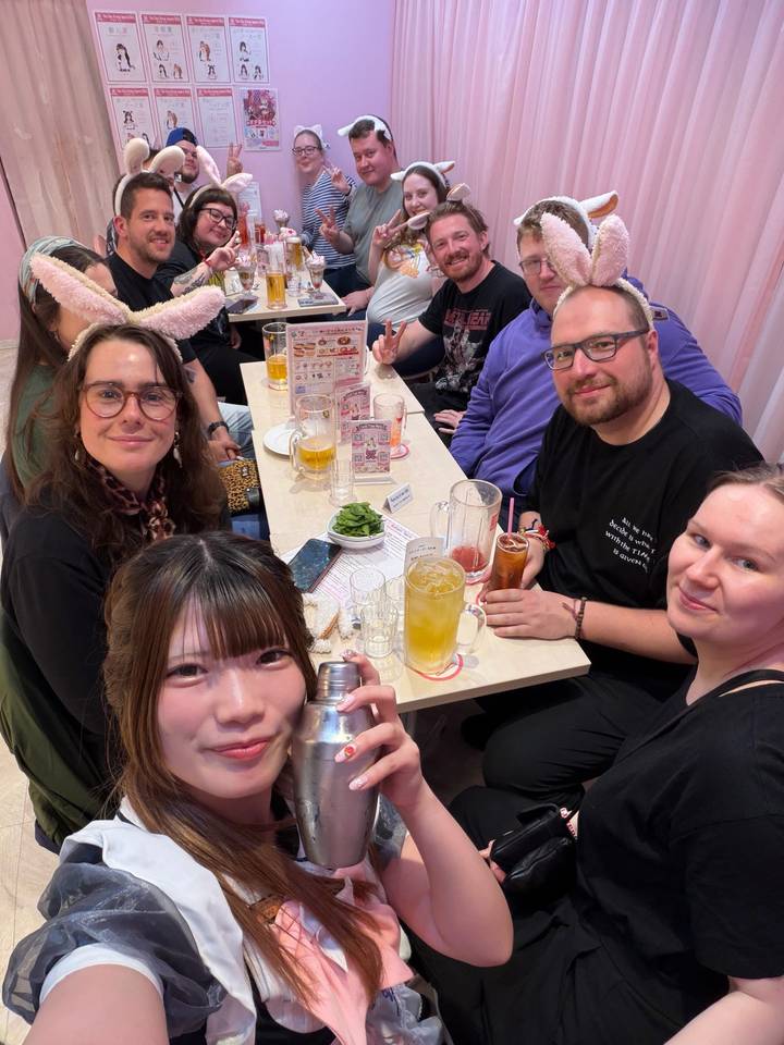 Friends gathered around a table of drinks and snacks in a brightly lit café.