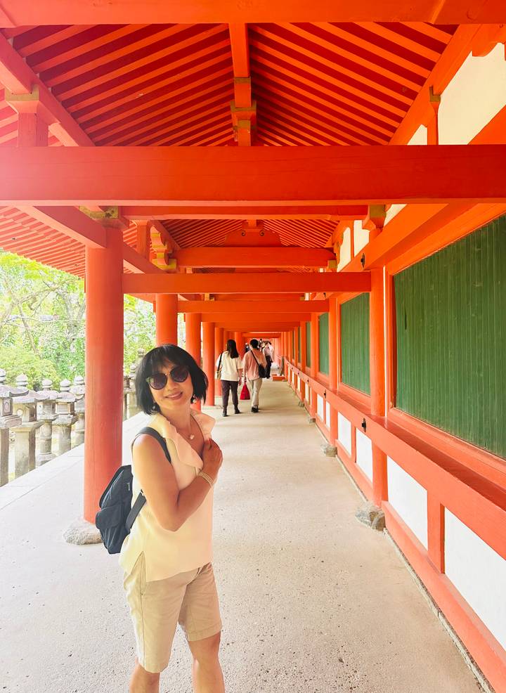 Smiling visitor stands in a long vermilion-painted corridor of a traditional Japanese shrine.
