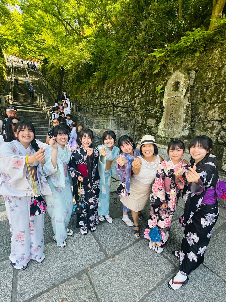 Tourist in hat poses with a group of local girls wearing colourful kimonos near stone temple steps.