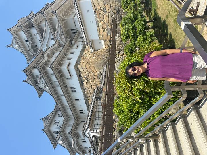 Visitor stands smiling in front of the imposing white towers and stone walls of Himeji Castle.