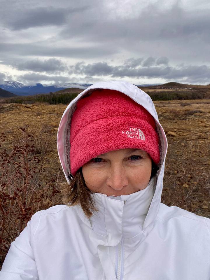 Close-up selfie of a bundled traveller with snowy mountains stretching across the horizon behind.