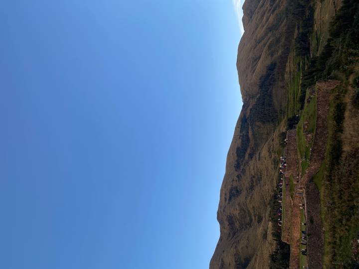 Low stone terraces and rolling hills sit beneath a vast blue sky in the Andean highlands.