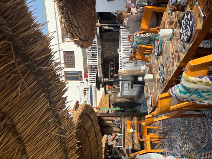 Open-air rooftop restaurant with wooden chairs, mosaic tile floor and straw canopies awaiting diners.