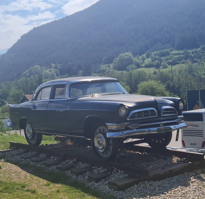 Vintage black sedan displayed on short railway track with misty green mountains rising behind.