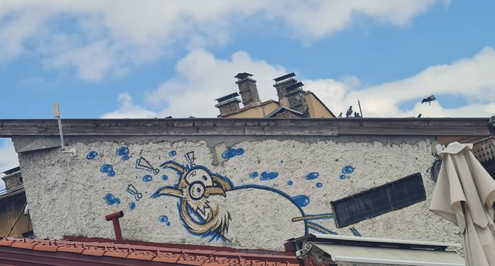 Blue cartoon bird graffiti painted on a rough white wall beneath a bright sky.