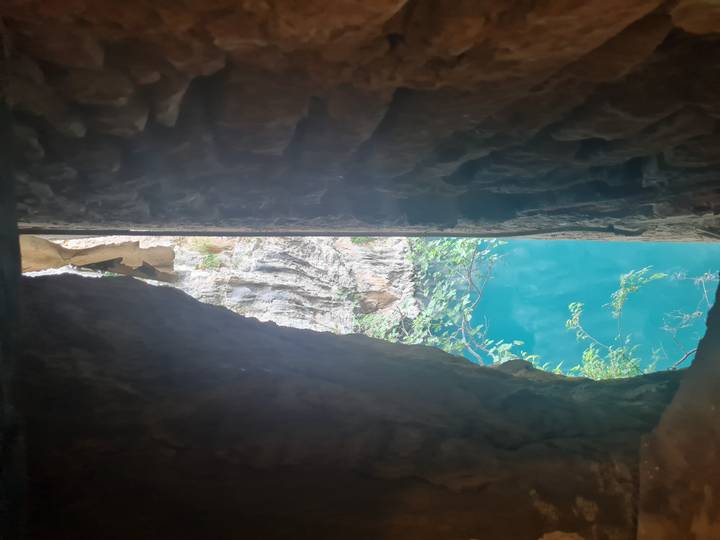 Narrow crevice in a limestone cliff opening onto bright turquoise water far below.