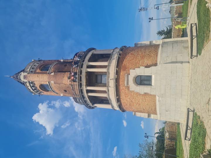 Brick Gardoš Tower with white stone base rises against blue sky as visitors look out from the balcony.
