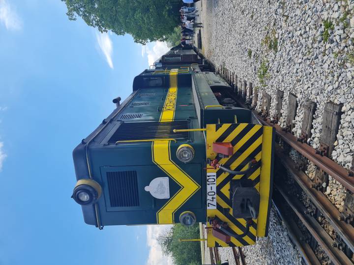Green and yellow diesel locomotive on narrow-gauge tracks under blue sky at a heritage railway.