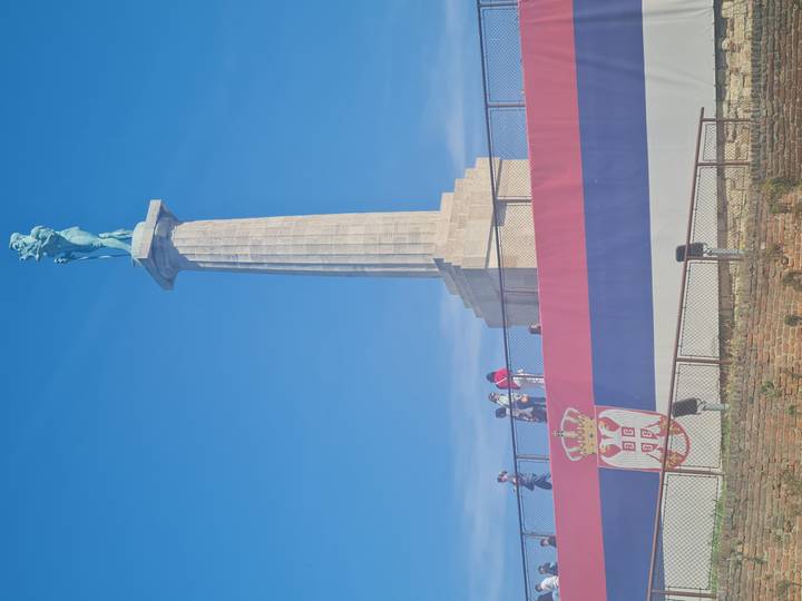 Tall stone column topped by the bronze Victor statue above a large Serbian flag mural at Kalemegdan Fortress.
