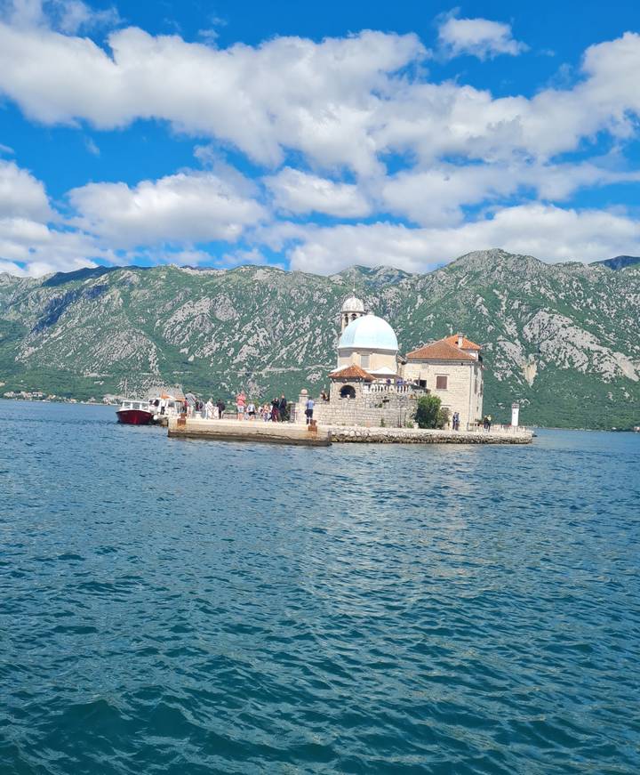 Boats dock beside tiny Our Lady of the Rocks church on a man-made island set against the green mountains of the Bay of Kotor.