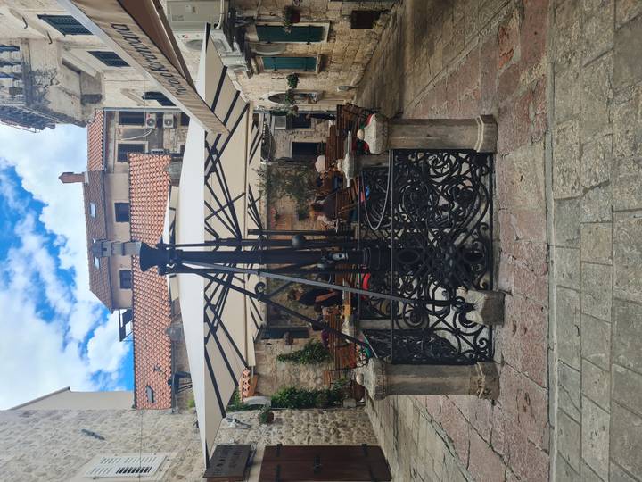 Stone courtyard café with wrought-iron well and umbrella-covered tables in a historic alley.