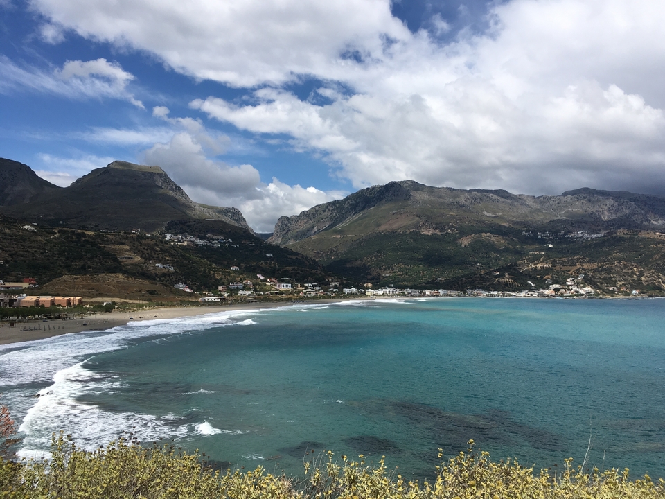 Village côtier entouré de montagnes et de mer bleue.