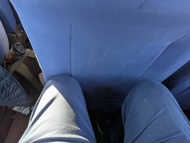 Passenger’s knees pressed against a tight bus seat with sunlight on trousers.