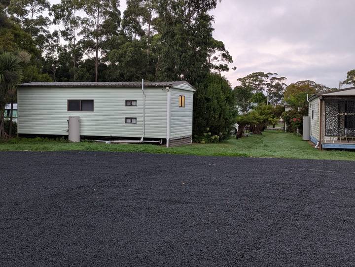 Simple prefab cabin beside a gravel road and green lawn in a holiday park.