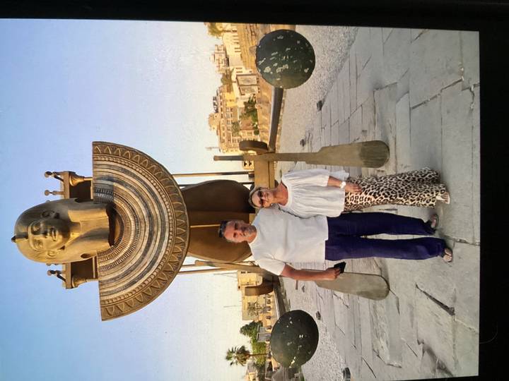 Couple stand before a large pharaoh bust and ornate barque statue in Luxor Temple courtyard.