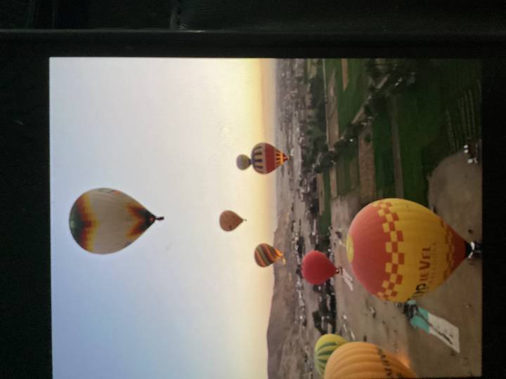 Colorful hot-air balloons drift over fields and desert terrain at sunrise in Luxor.