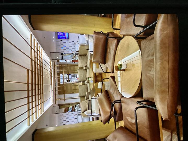 Modern lounge area with tan leather chairs and a sleek wooden coffee table under geometric ceiling lights.